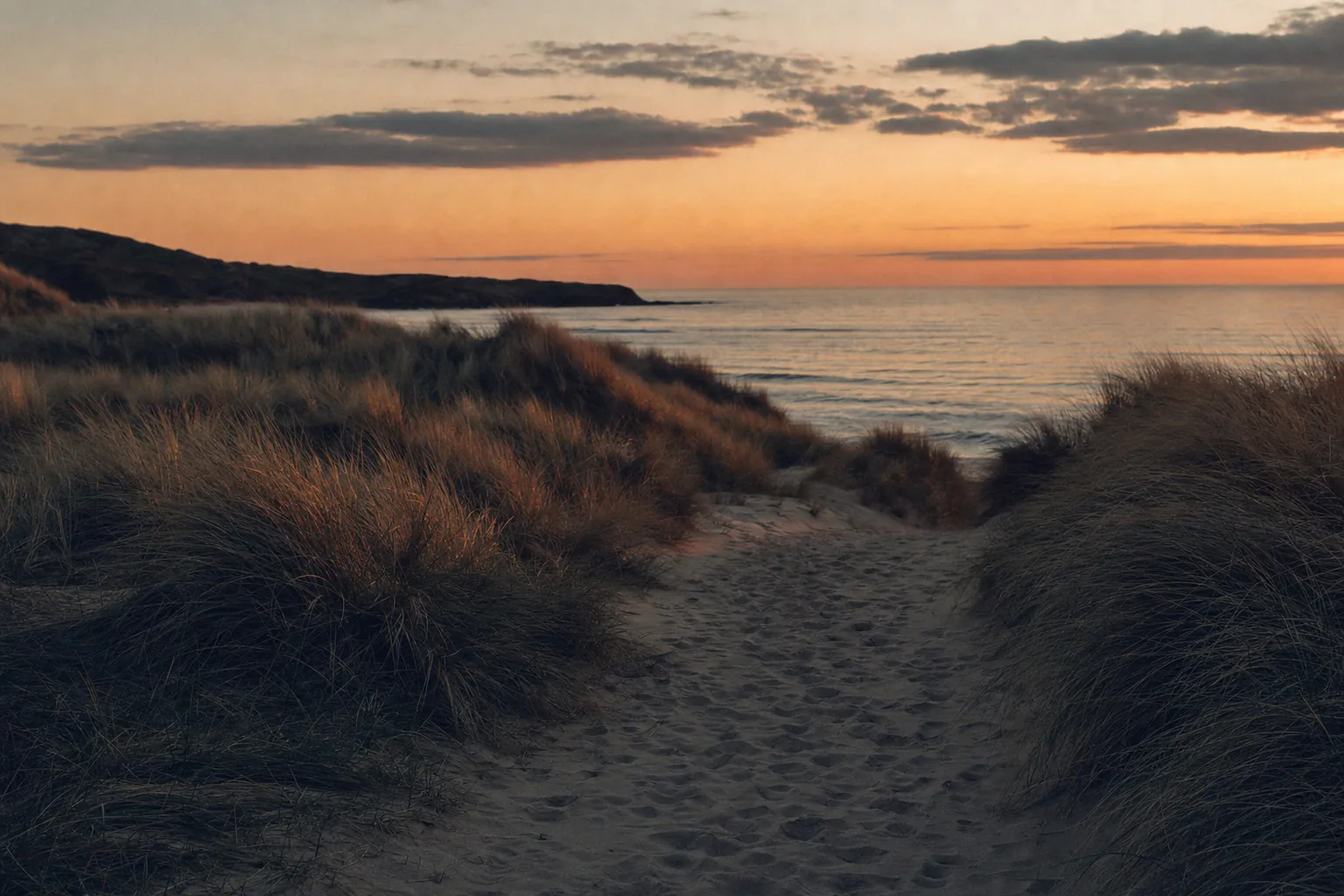 A sand path worn through marram grass, opening onto the open sea at dusk (example photo)
